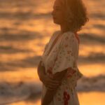 A serene silhouette of a woman in a floral dress by the ocean during a calming sunset.